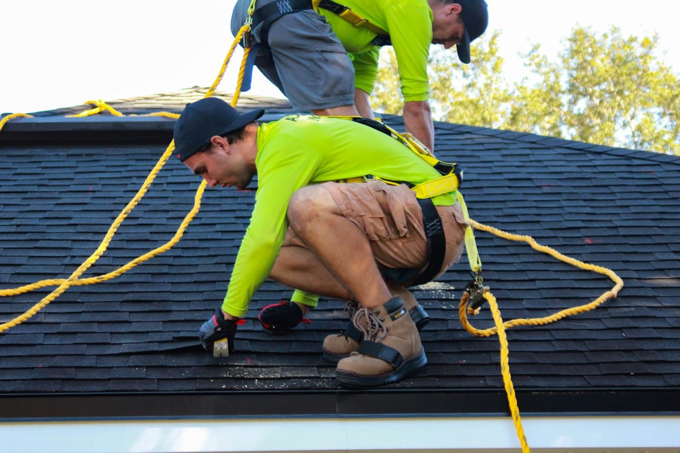 Roofers in safety harnesses installing asphalt shingles on a residential roof